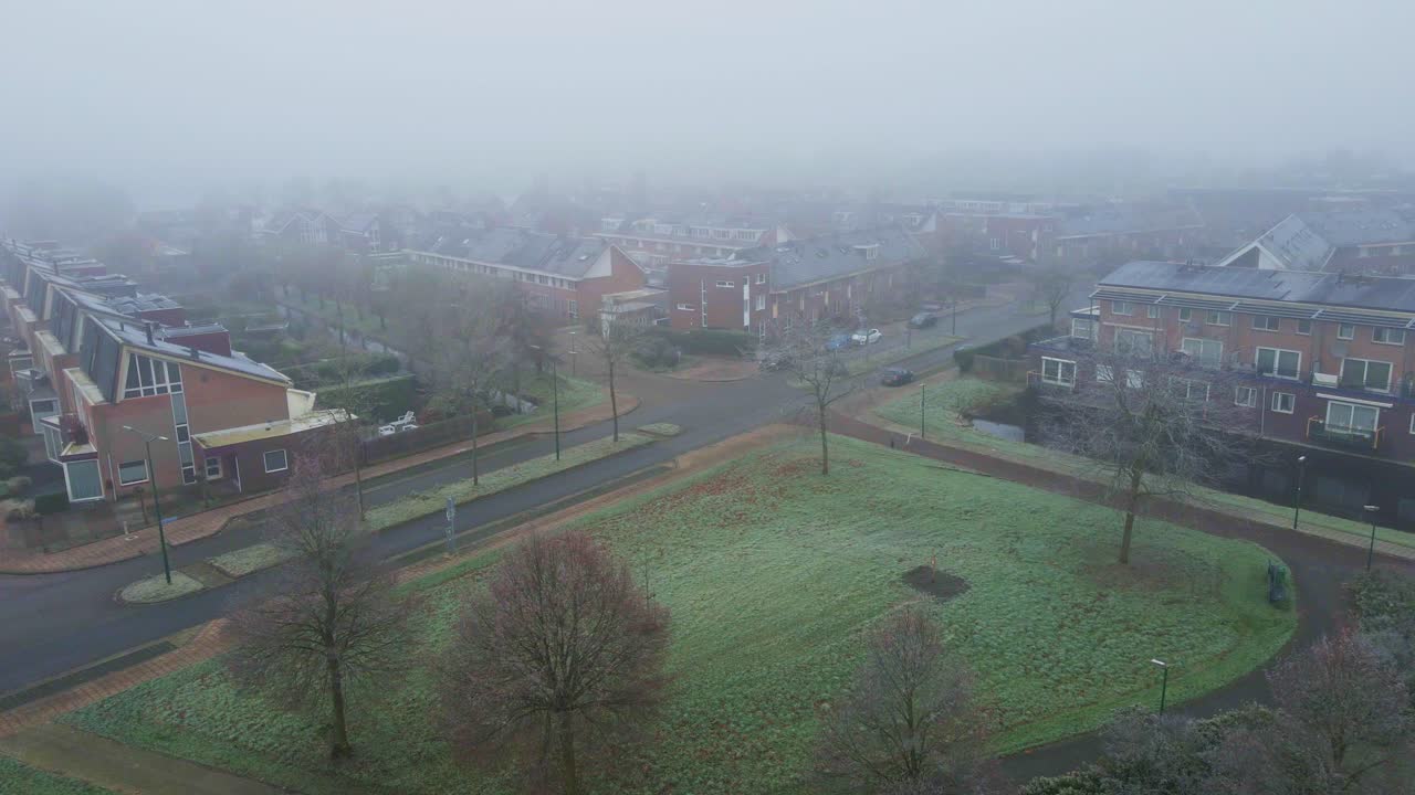 dron volando bajo de parque brumoso cerca de un barrio suburbano cubierto de niebla