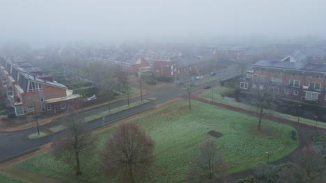 drone flying low of misty park near a suburban neighborhood covered in mist