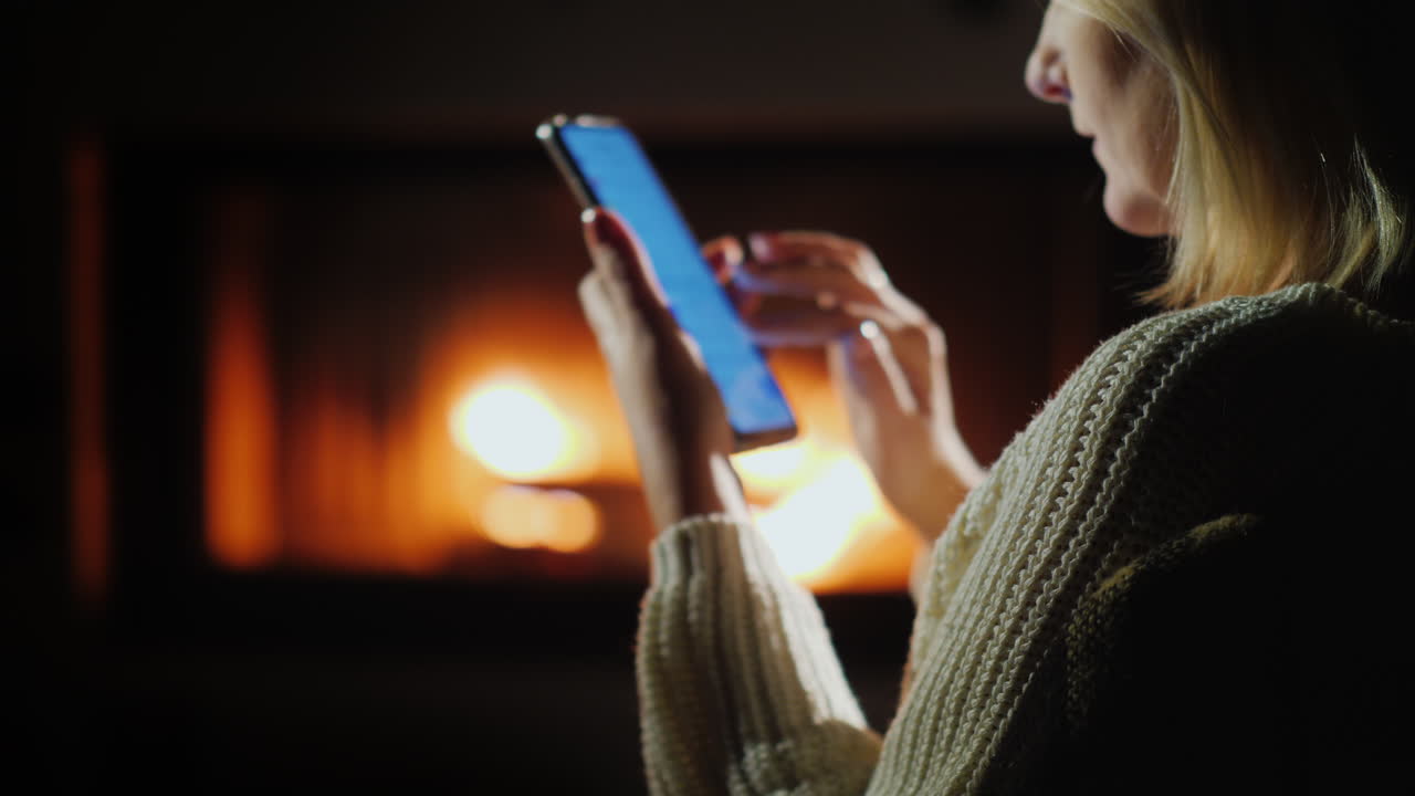 Giovane donna usa uno smartphone mentre è seduta accanto al caminetto