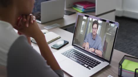 sección media de una mujer afroamericana haciendo una videollamada con un colega masculino en una computadora portátil en la oficina