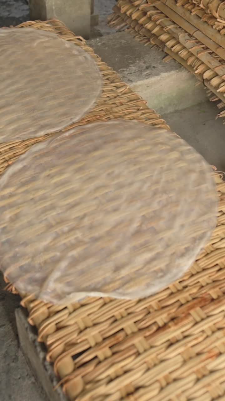 Schermo verticale. Due fogli di riso che si asciugano su una stuoia intrecciata, cerchi traslucidi affiancati su stendini di bambù, lieve luce solare e flusso d'aria delicato, produzione familiare in piccoli lotti in un laboratorio tradizionale