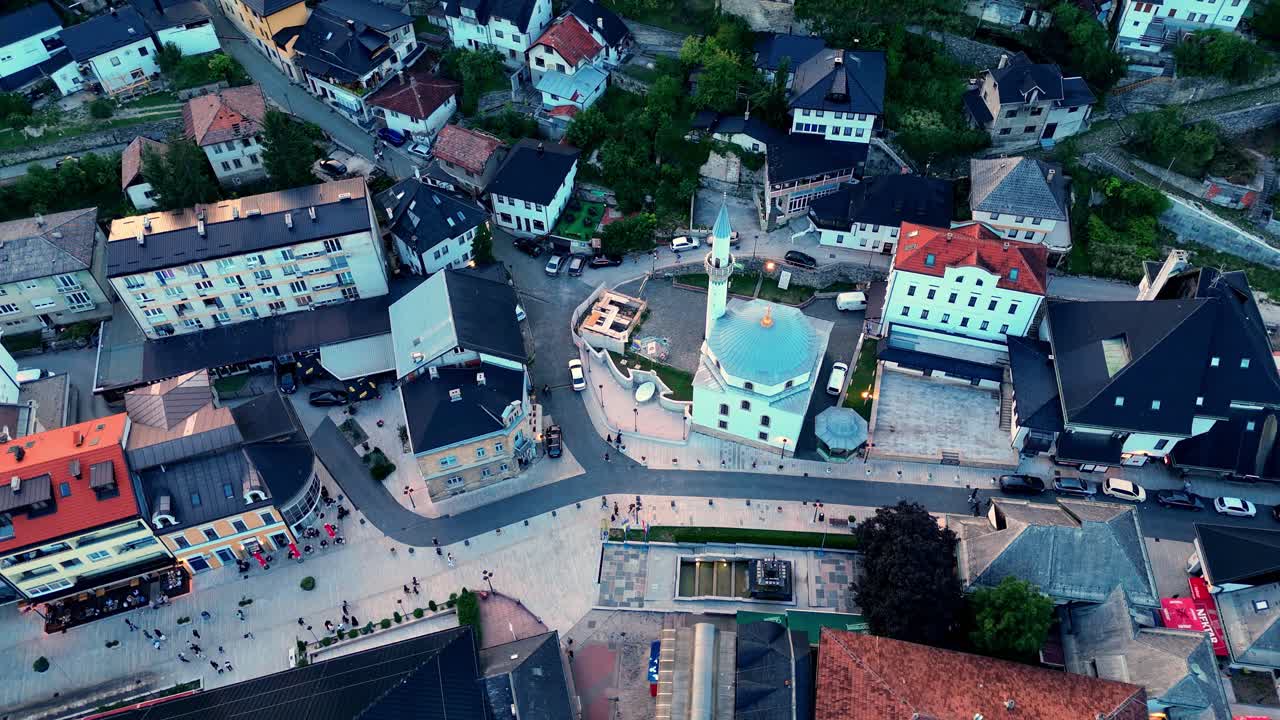 Aerial drone view of a small mosque in Bosnia and Herzegovina, surrounded by colorful houses and narrow streets of the old town at sunset, symbol of local culture and faith