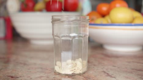 bulk sliced or flaked organic almonds being poured in a glass jar on a kitchen table