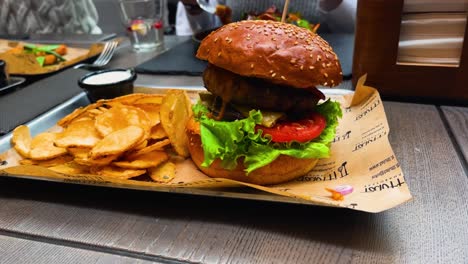 close-up shot of a juicy beef burger with lettuce and a slice of tomato with a side of fresh potato chips, sitting on a plate in the restaurant, parallax shot