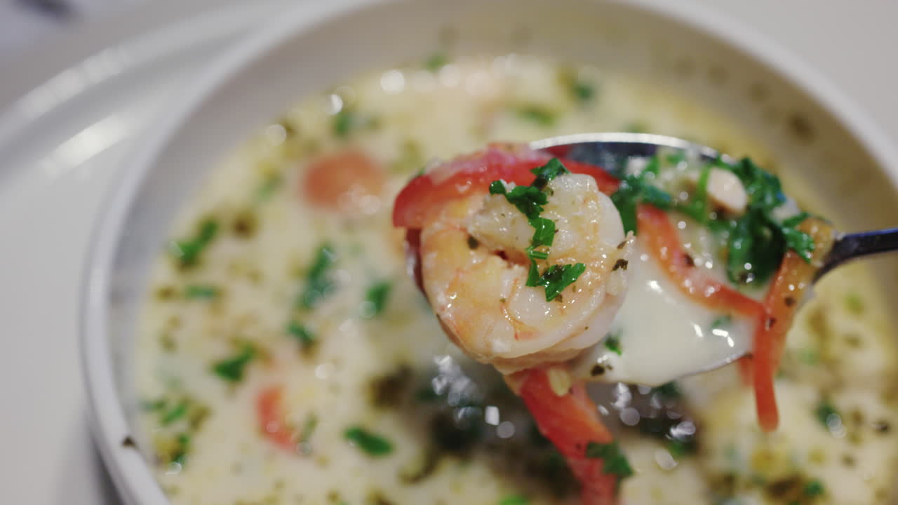 Primer plano de un camarón que se saca con una cuchara de una sopa con hierbas y verduras.
