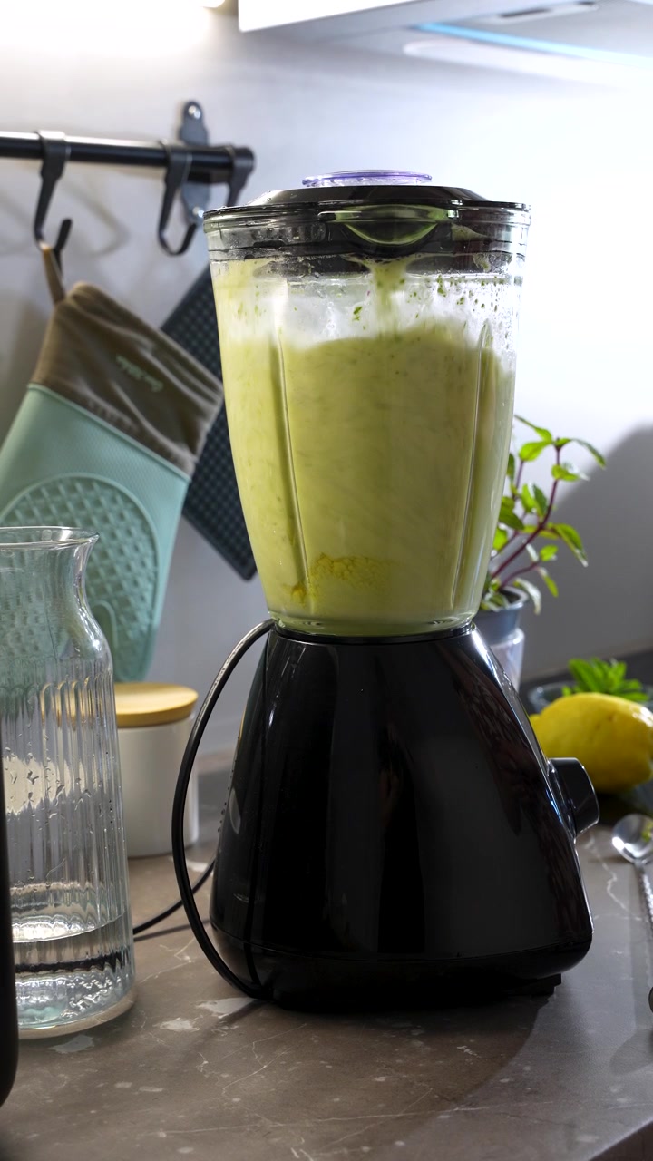 Video verticale di una donna che prepara limonata fresca alla menta in un frullatore. Primo piano della preparazione di una bevanda salutare in un ambiente cucina moderno e luminoso.