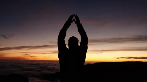 silhouette of a man lifting his arms above his head during sunset at pico do arieiro, madeira, portugal.