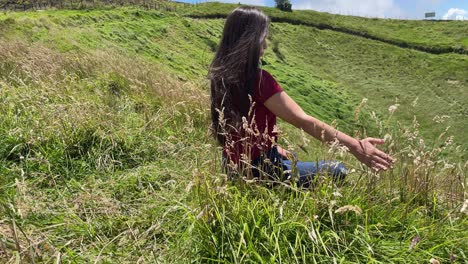 brunette woman playing with long grass sitting on scenic hillside overlooking lagoon in costa rica 4k