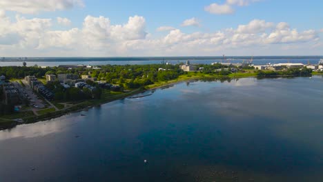 aerial drone footage flying lower and descending in front of a gorgeous sunny peninsula at paljassaare estonia while a shipyard port harbor and landscape is in the horizon with blue baltic ocean water