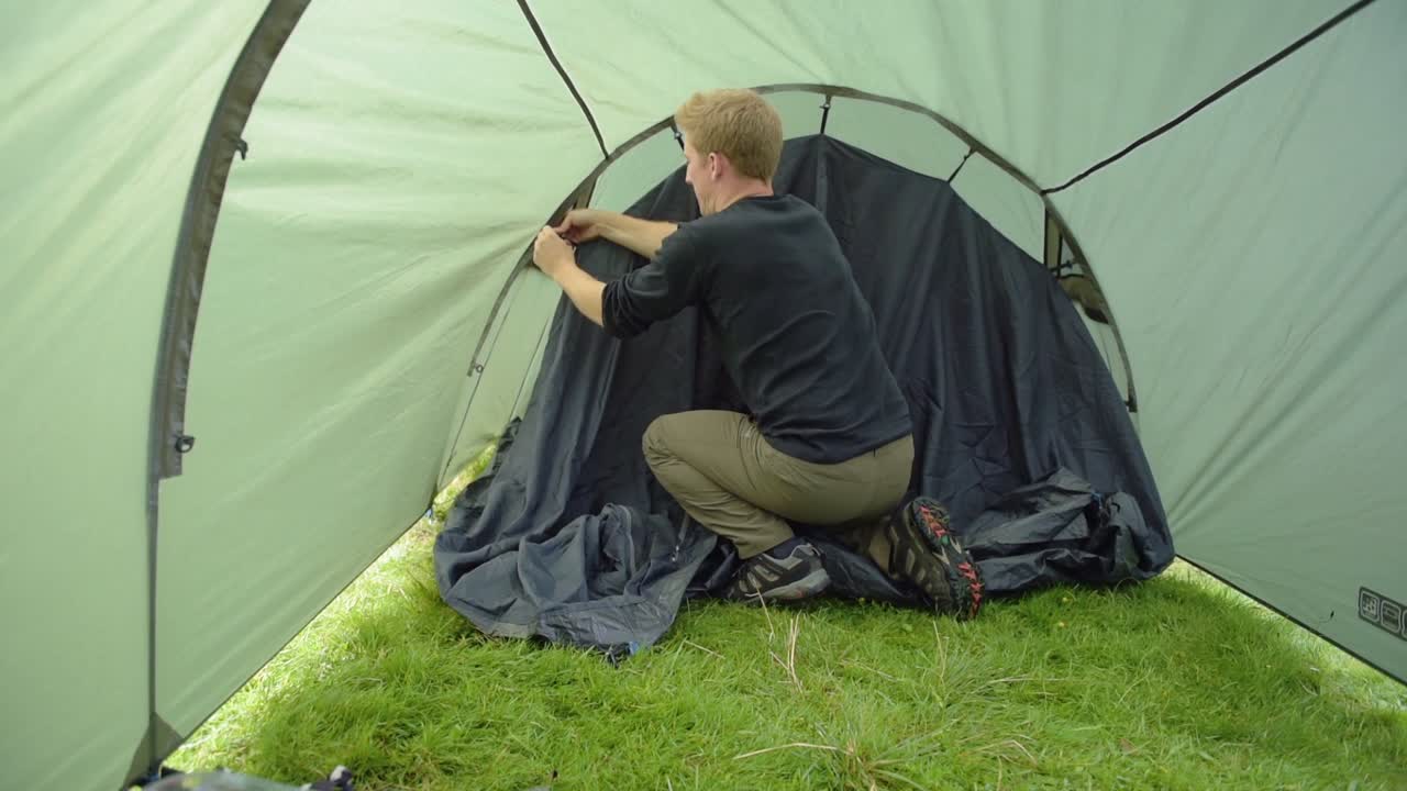 A Man Fixing The Inside Of The Tent Along The Coast Of Loch Lochy And Caledonian Canal For Camping Located In Lochaber, Highland, Scotland. -medium shot