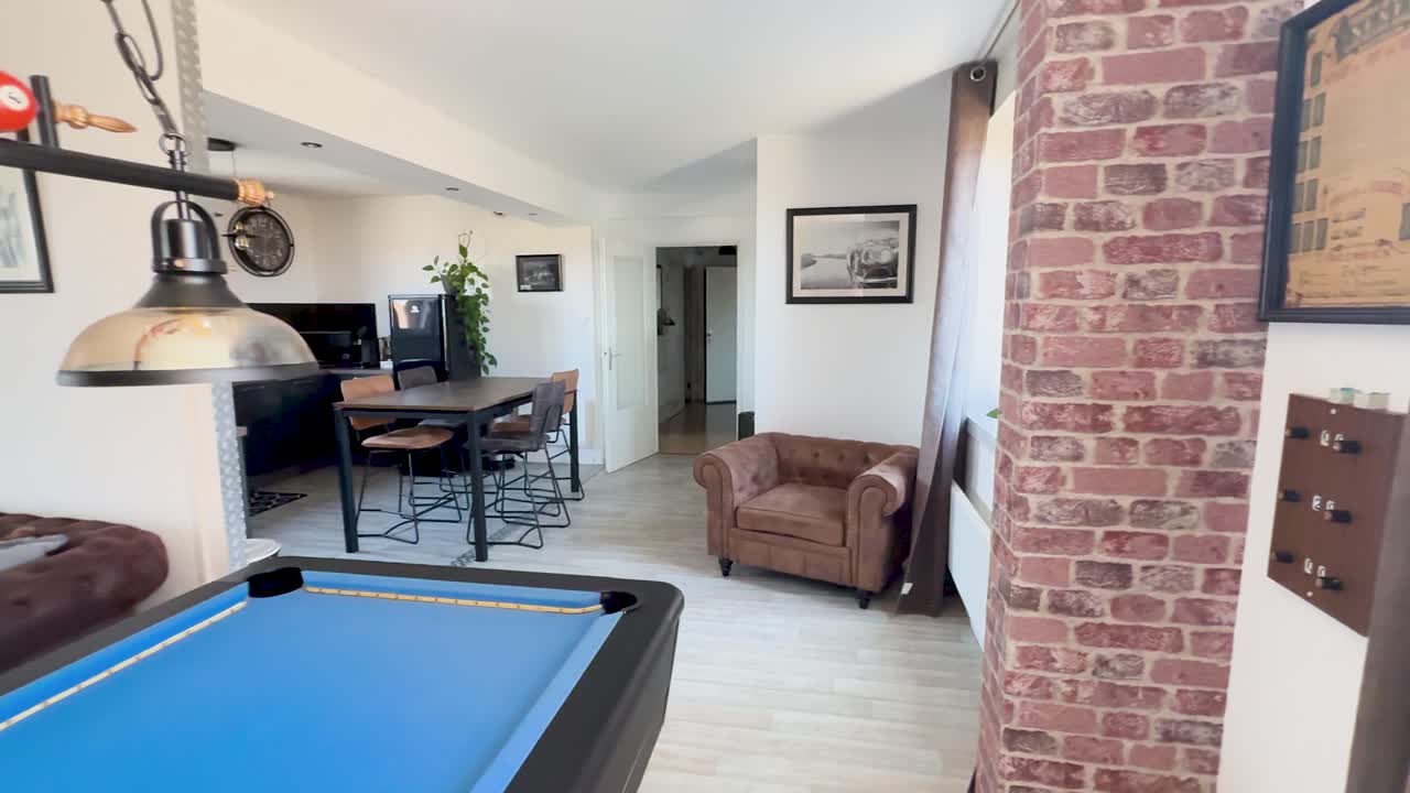 Camera smoothly pans through a bright, retro-inspired apartment lounge featuring a blue pool table, vintage decor, and cozy seating under natural daylight