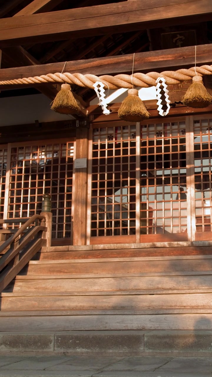 Sollys fra den gyldne time oplyser træfacaden og shimenawa-rebet på en japansk shinto-helligdom