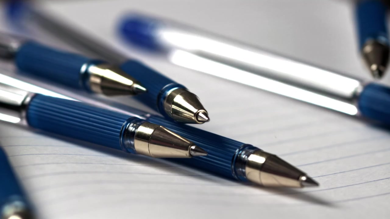 Penne a sfera blu che cadono su una pagina di quaderno a righe.