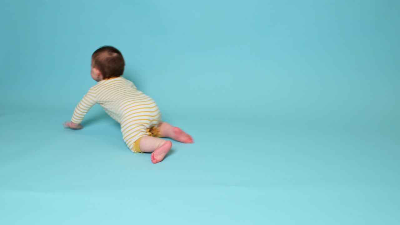 niño feliz niño pequeño está jugando con una pelota en un fondo azul de estudio. niño sonriente lanza una pelota al suelo, niño de diez meses de edad