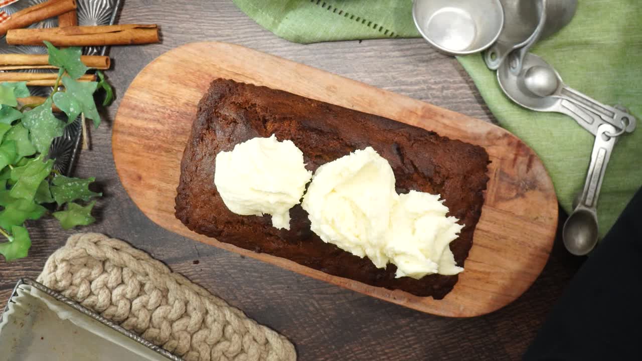 Baking a carrot cake loaf with cream cheese icing and topped with roasted salted pecans. Making a Autumn dessert with carrots, flour, sugar, nuts and frosting. Spreading icing on the cake.