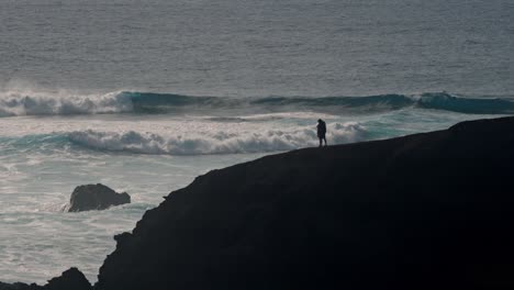 a young couple walks hand in hand along a rugged volcanic cliff overlooking the atlantic ocean in lanzarote, canary islands, spain.