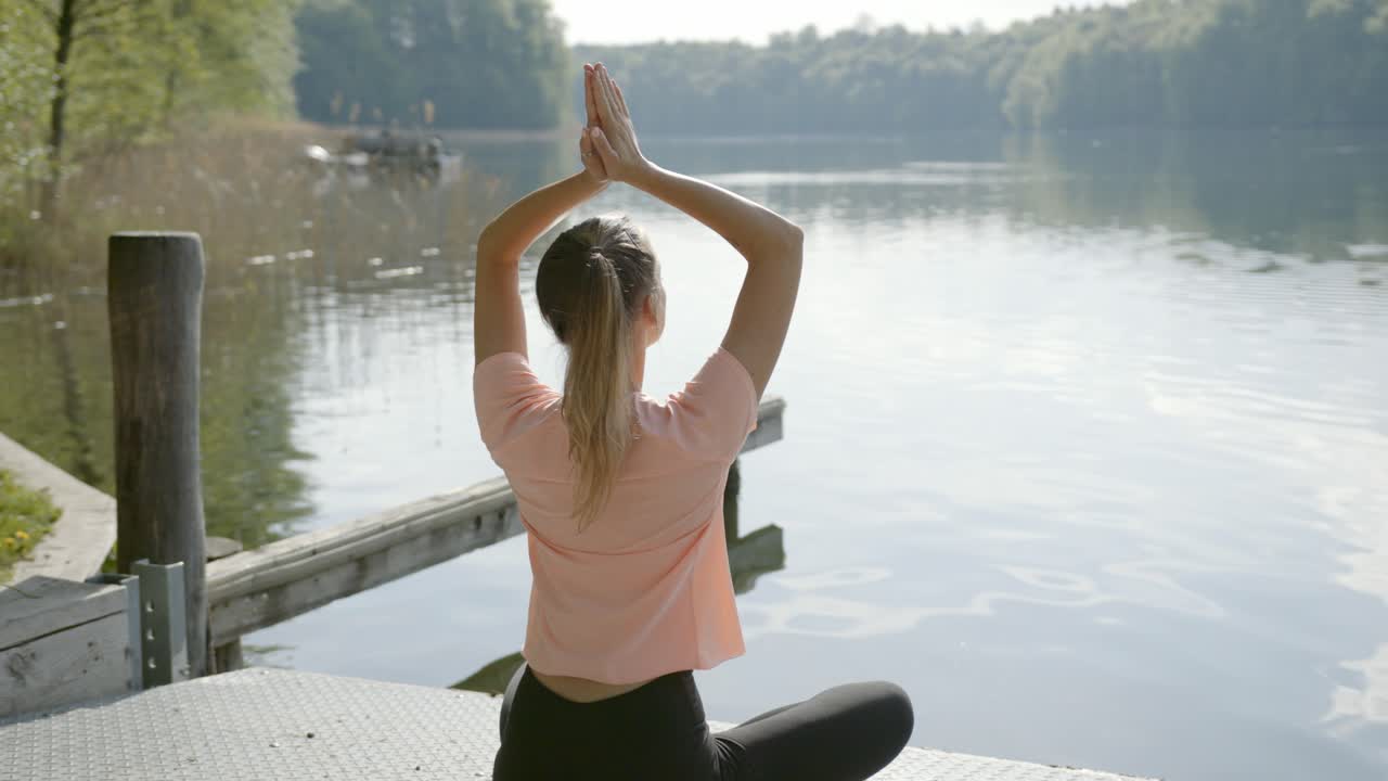 mujer levanta los brazos por encima de la cabeza y comienza a mediar junto al lago