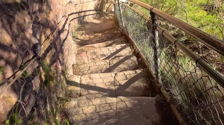 Prospettiva in prima persona che scende ripide scale di arenaria con ringhiere metalliche nel Parco Nazionale delle Blue Mountains.