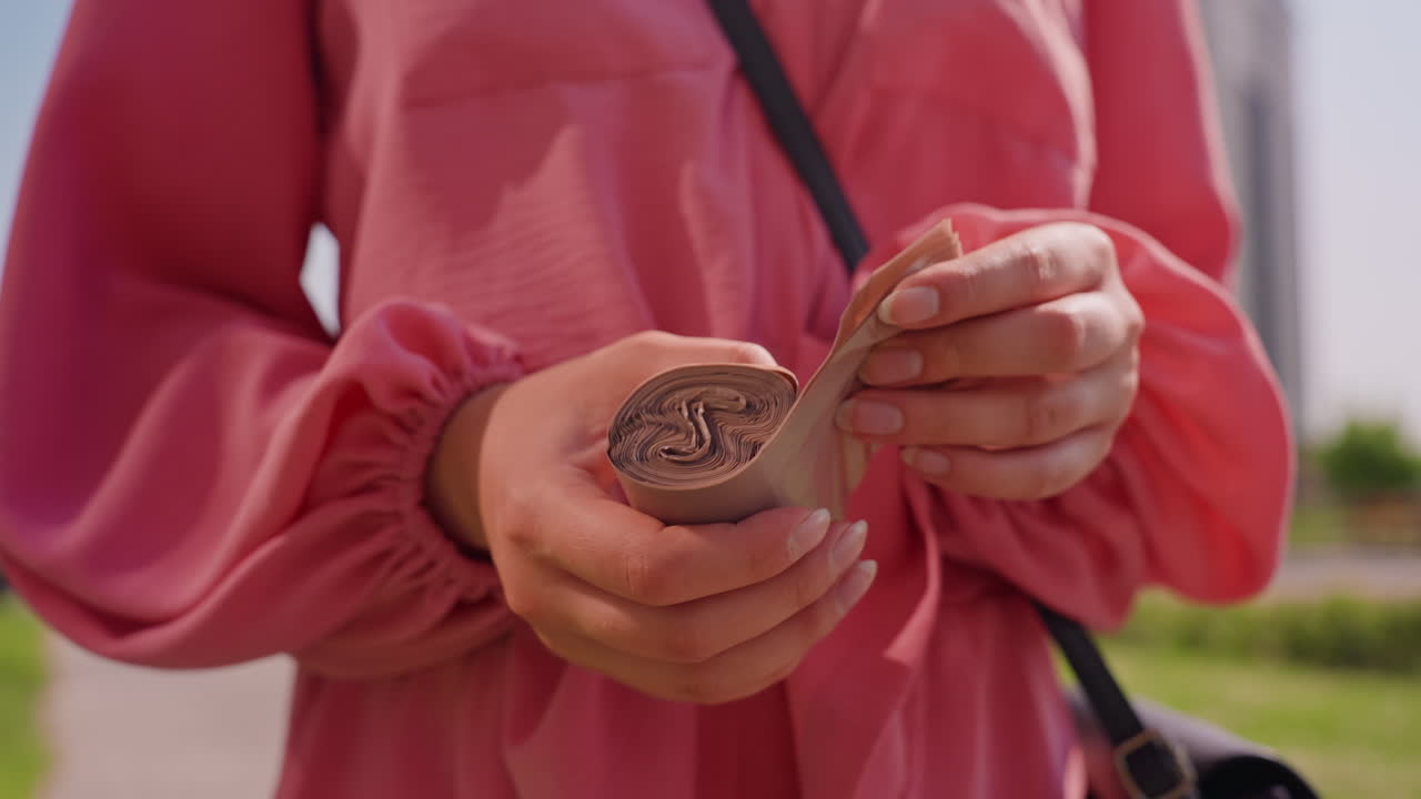 Hands Open Chocolate Coin With Knife, Careful Peel Of Foil Wrapping From HeartStamped Candy CloseUp Of Fingers And Pink Jacket Sleeve, Outdoor Park Background, Casual Snack Moment, Summer Light