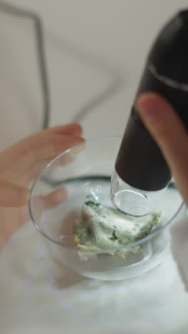 little girl scientist scans plant leaf in bowl with digital probe doing experiment at table in biochemical laboratory extreme close view