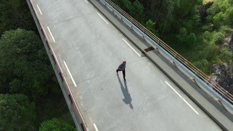 man jogging on bridge over ocean fjord in western norway - aerial birds eye follow with fjord seen far down below