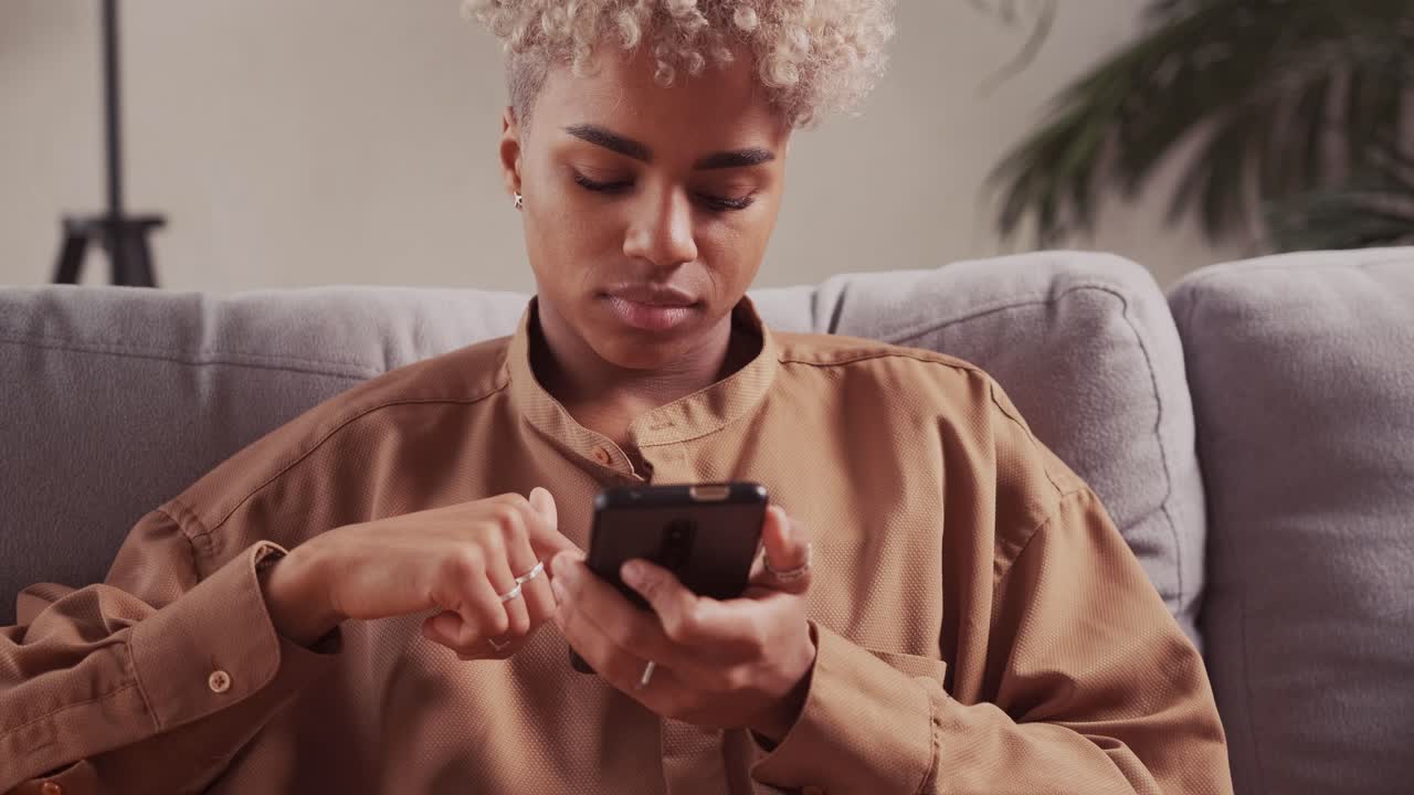 African woman rest on sofa use smartphone at home sofa