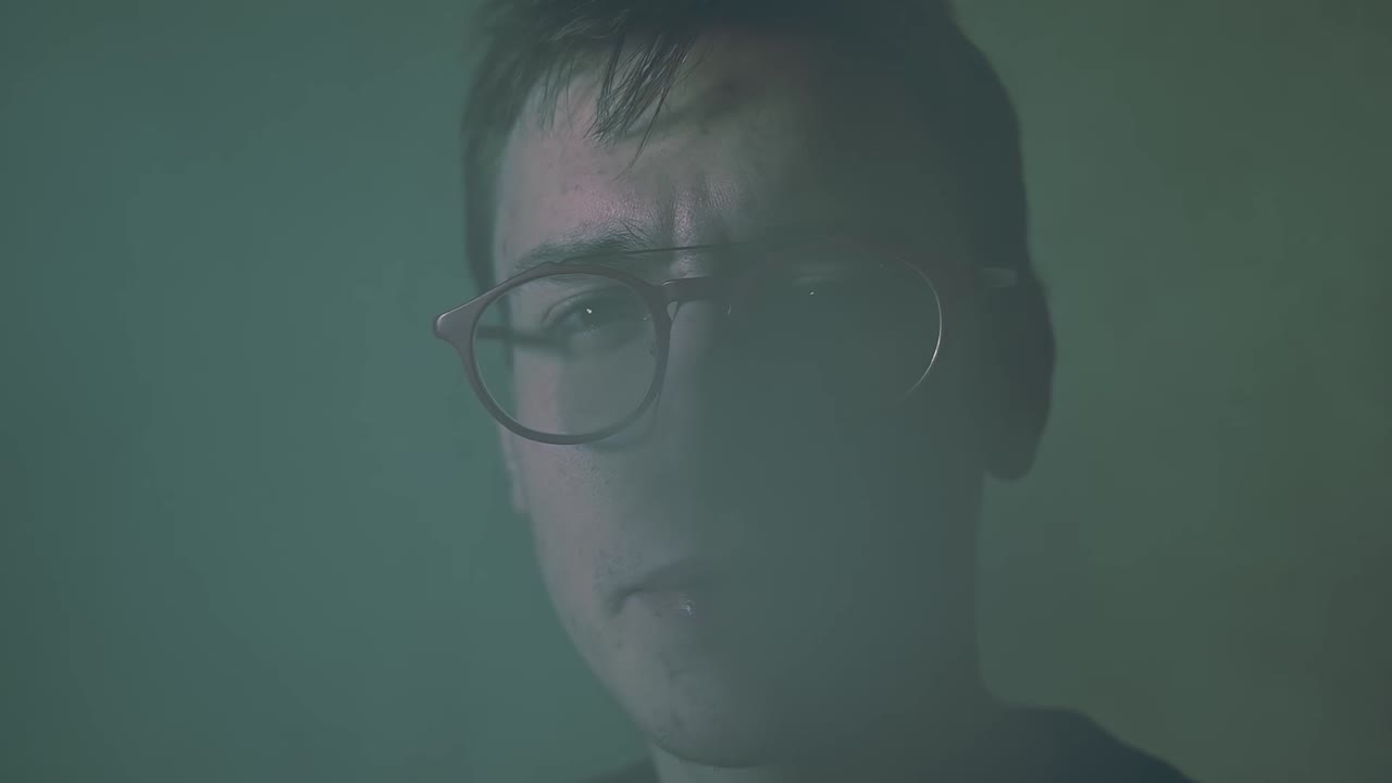 Young man with red glasses vaping and exhales smoke in the camera. Close up. Slow motion