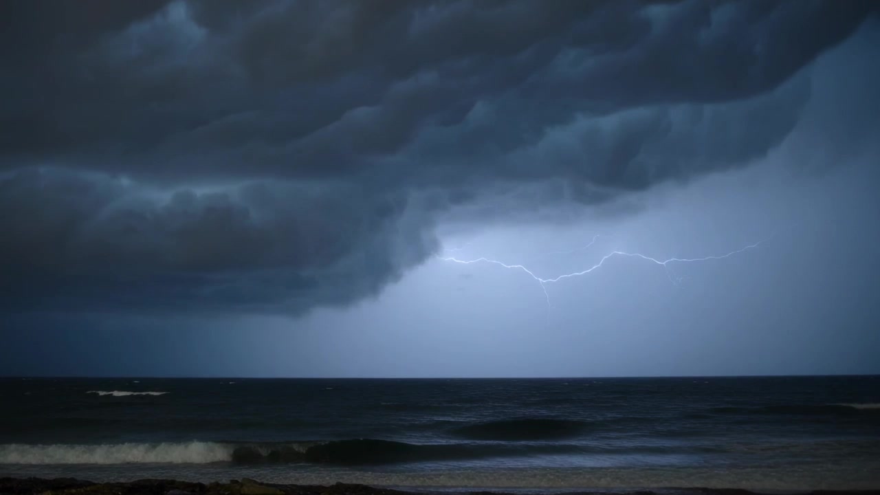 Advancing storm with shelf cloud sparking lightning over night shoreline, lighting ocean and rain
