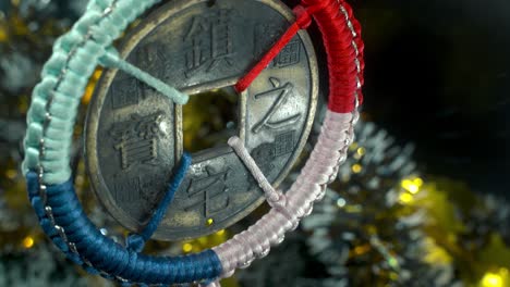 dreamy close-up shot of a chinese ancient traditional lucky coin, asian new year decoration, shiny blur christmas background, square hole colorful strings, culture holyday symbol, smooth tilt up 4k