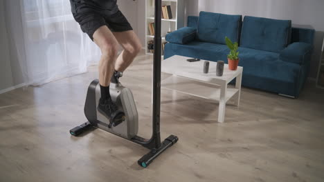 male legs on stationary bike in living room adult man is training alone for health and good physical condition details shot of body