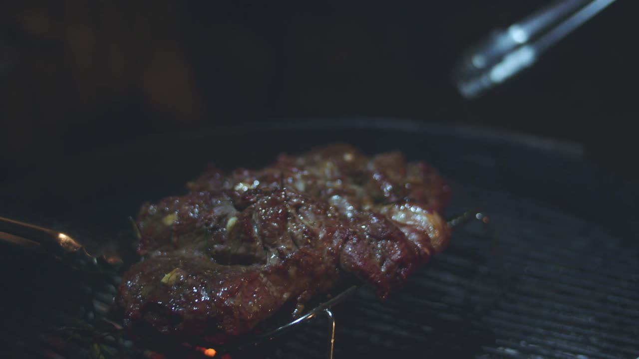 두 세트의 집게가 뜨거운 석탄 위의 바비큐에 버터플라이 양고기를 던집니다.