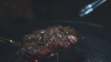 two sets of tongs toss a butterflied lamb on the barbeque over hot coals