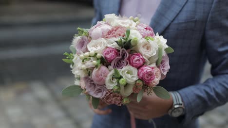 Groom-with-wedding-bouquet-in-his-hands-on-the-street.-Pink-shirt,-blue-jacket