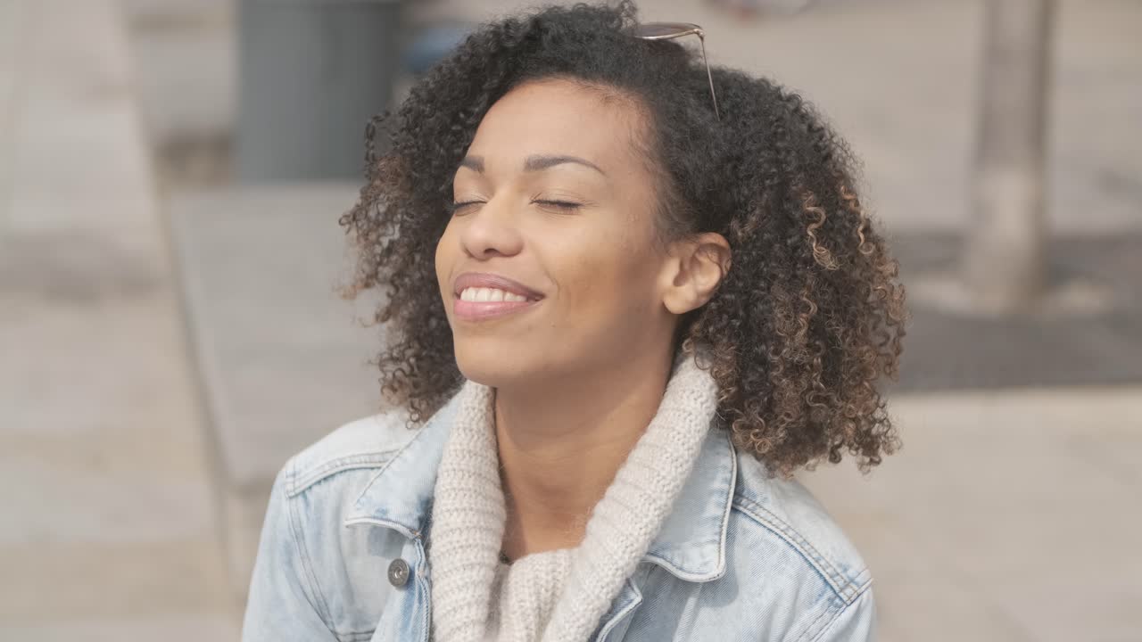 Beautiful girl with afro haircut sitting on bench at city street