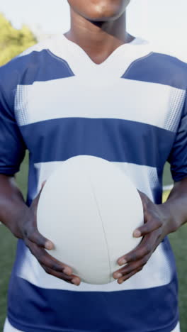 vertical video: rugby player holding ball on field, wearing blue and white jersey