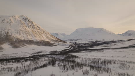 frozen river through snowy mountain valley landscape in norway, aerial