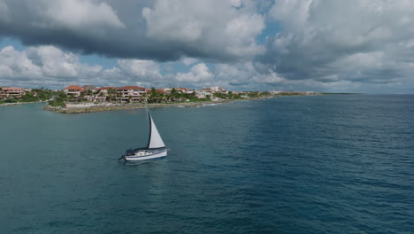 an stunning rotation aerial shot of a sailing yacht leaving the shoreline, revealing a stunning holiday apartment building with a picturesque seashore in the foreground in puerto avenuras, mexico