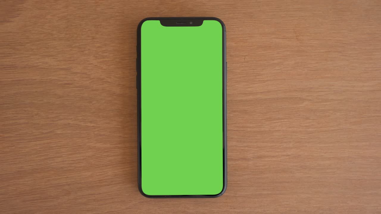 el teléfono inteligente se coloca en la mesa de madera, el teléfono de pantalla verde, el teléfono móvil de pantalla cerrada con maqueta, el monitor de llave cromática, el teléfono celular en close-up en el escritorio marrón, el teléfono inteligente de maqueta, la vista superior del deslizador.