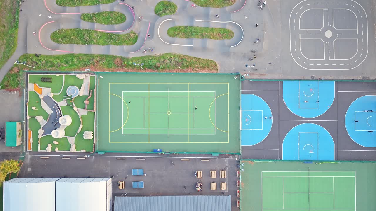 Top down footage revealing colorful tennis, basketball and traffic courts with playgrounds at Hillsborough Park, Sheffield, South Yorkshire, England with Residential area visible in background