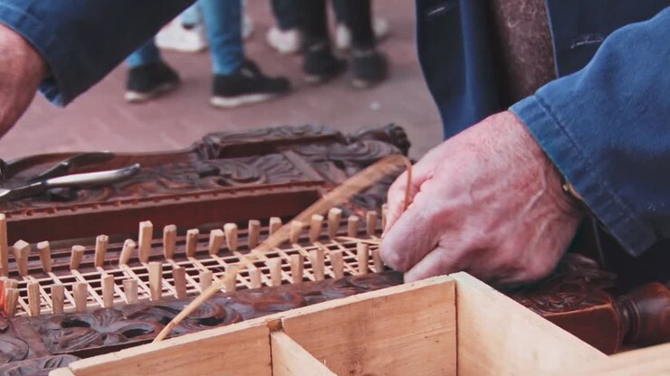 Close up old carpenter hands in workshop weave wicker net in to chair with tiny hamer and wedge