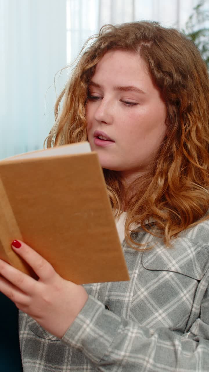 Woman sitting on sofa opening and reading book with focus thoughtfully flipping pages and reflecting