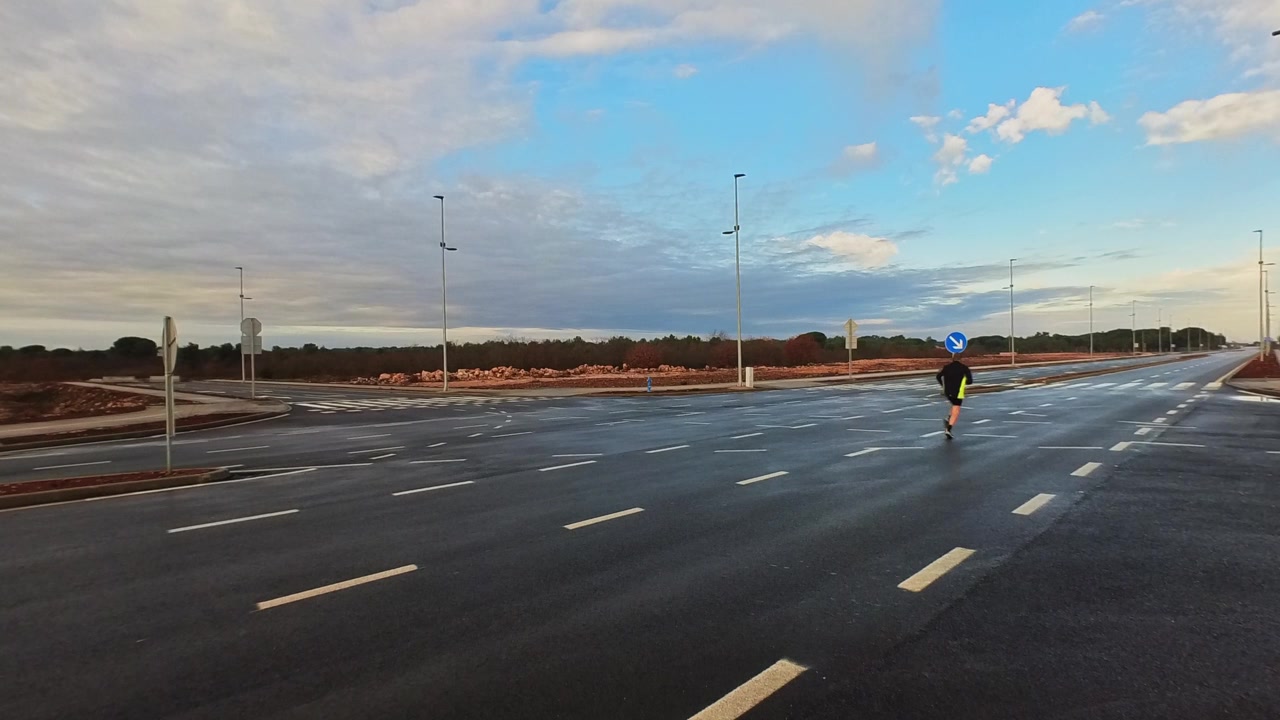 Bredt skud af en atlet, der jogger væk på en stor, tom motorvej under solopgang. Dramatisk skyet himmel. Koncept for udholdenhed, personlige mål og frihed.