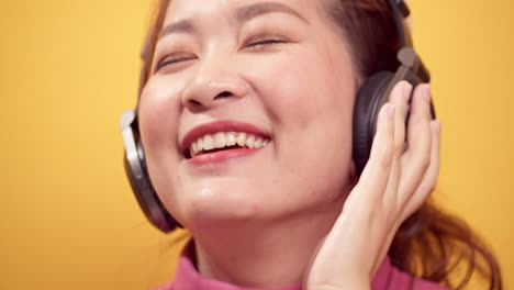 brunette young asian woman happy listening to music on headphones with relaxed on bright yellow background