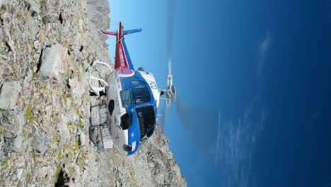 Helicopter-with-spinning-rotors-on-rocky,-alpine-terrain