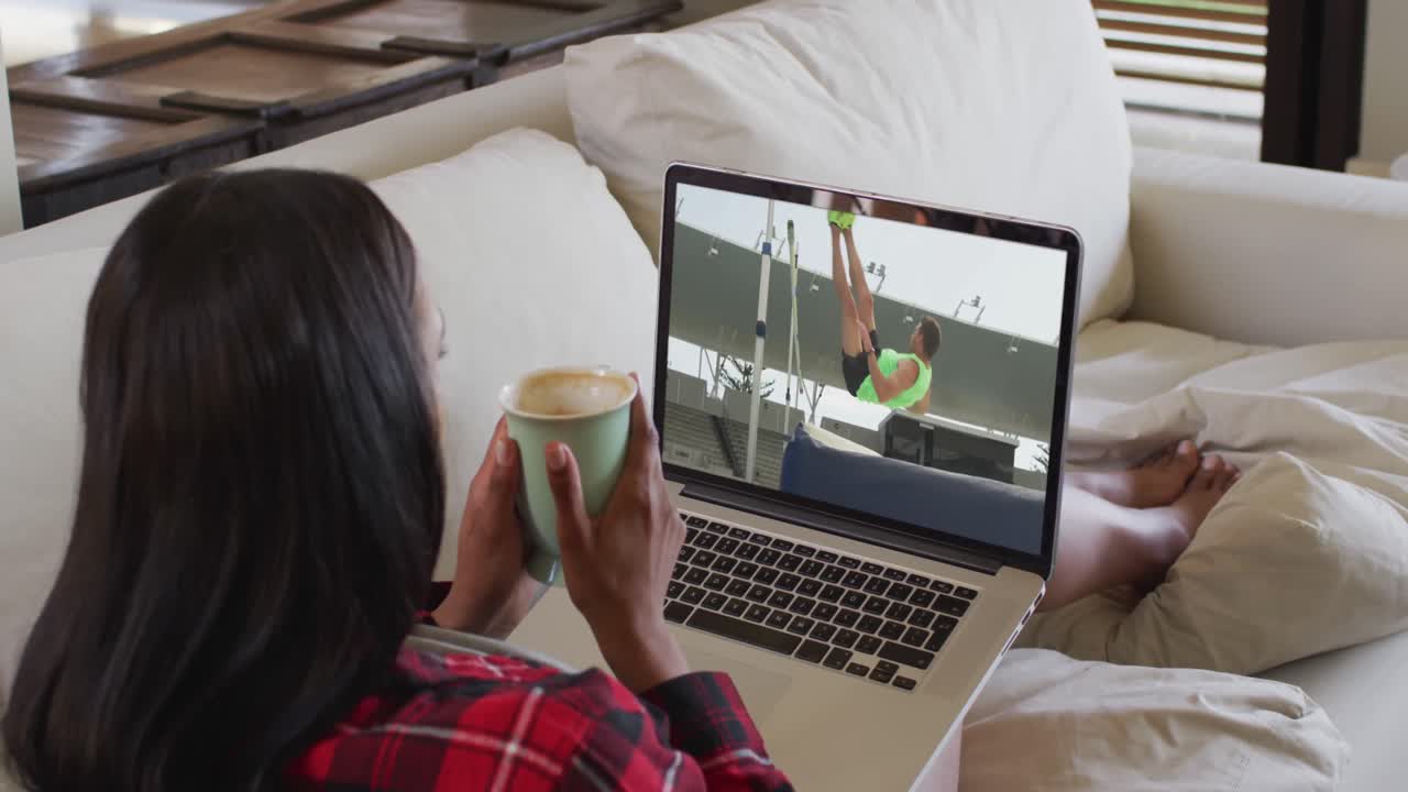 Composite of woman sitting at home holding coffee watching athletics high jump event on laptop