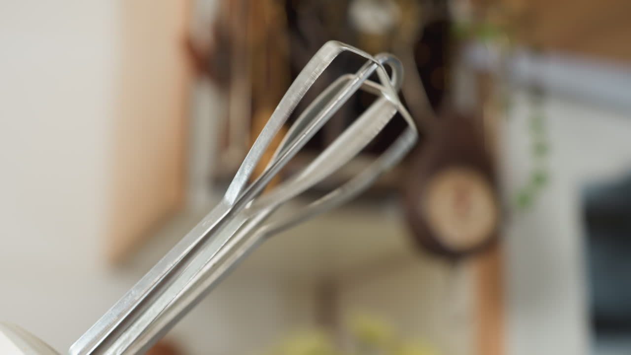 Close up of electric mixer whisk attachment rotating rapidly during mixing process in kitchen setting, showing motion blur from speed with soft background of utensils