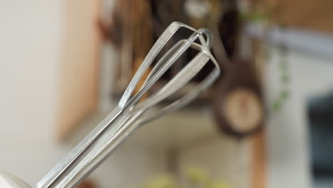 close up of electric mixer whisk attachment rotating rapidly during mixing process in kitchen setting, showing motion blur from speed with soft background of utensils