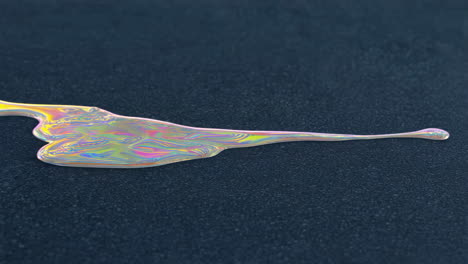 iridescent liquid spilling on a dark textured surface