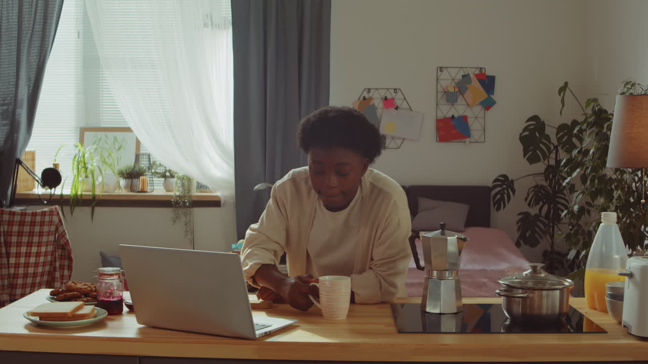 mujer afroamericana bebiendo café y usando una computadora portátil en casa