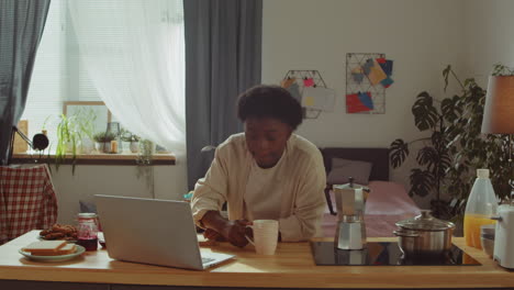 african american woman drinking coffee and using laptop at home